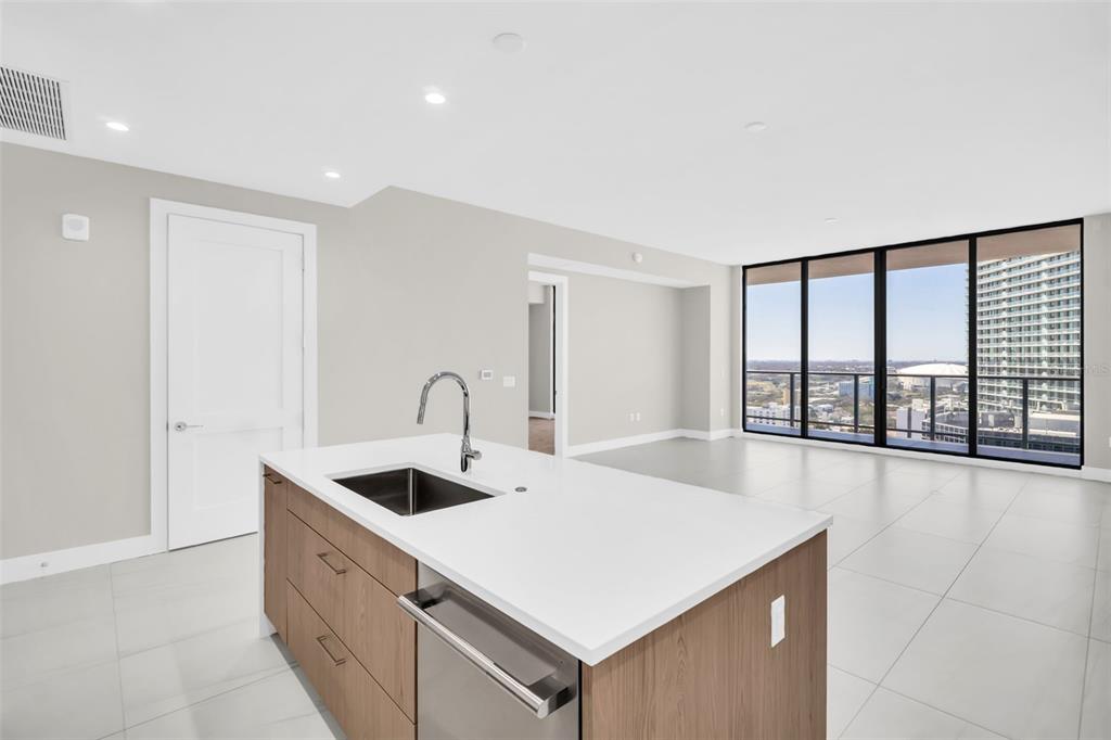 A modern kitchen island with a sink and light wood cabinets faces a bright living area — 275 1ST AVENUE S UNIT 2708, ST PETERSBURG, FL