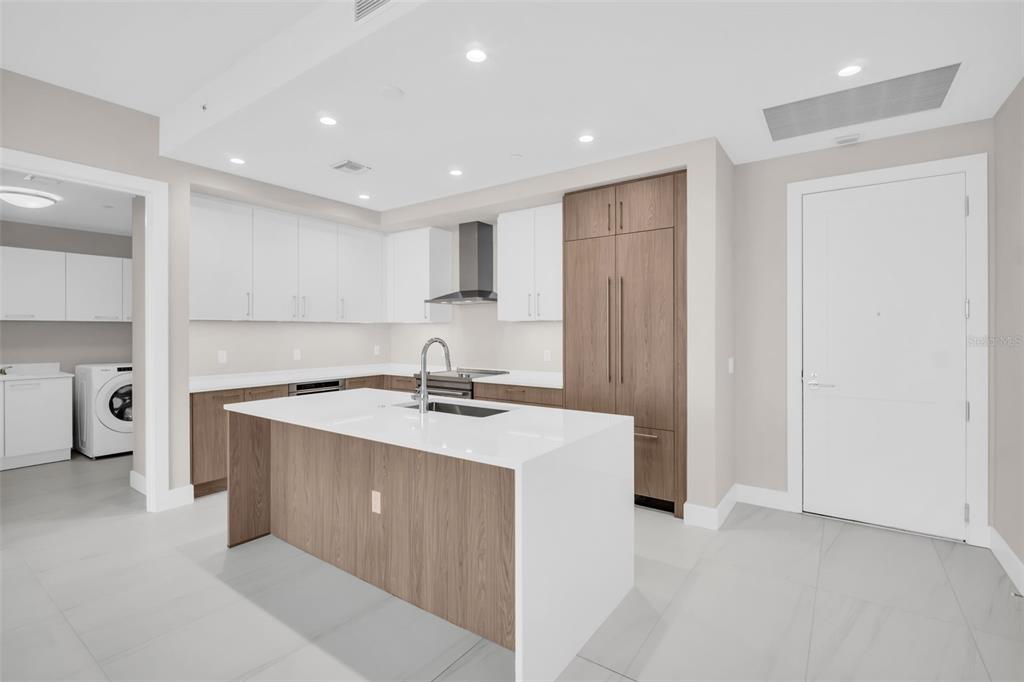 A modern kitchen features white upper cabinets, wood-paneled lower cabinets, a white island, and tile flooring — 275 1ST AVENUE S UNIT 2708, ST PETERSBURG, FL