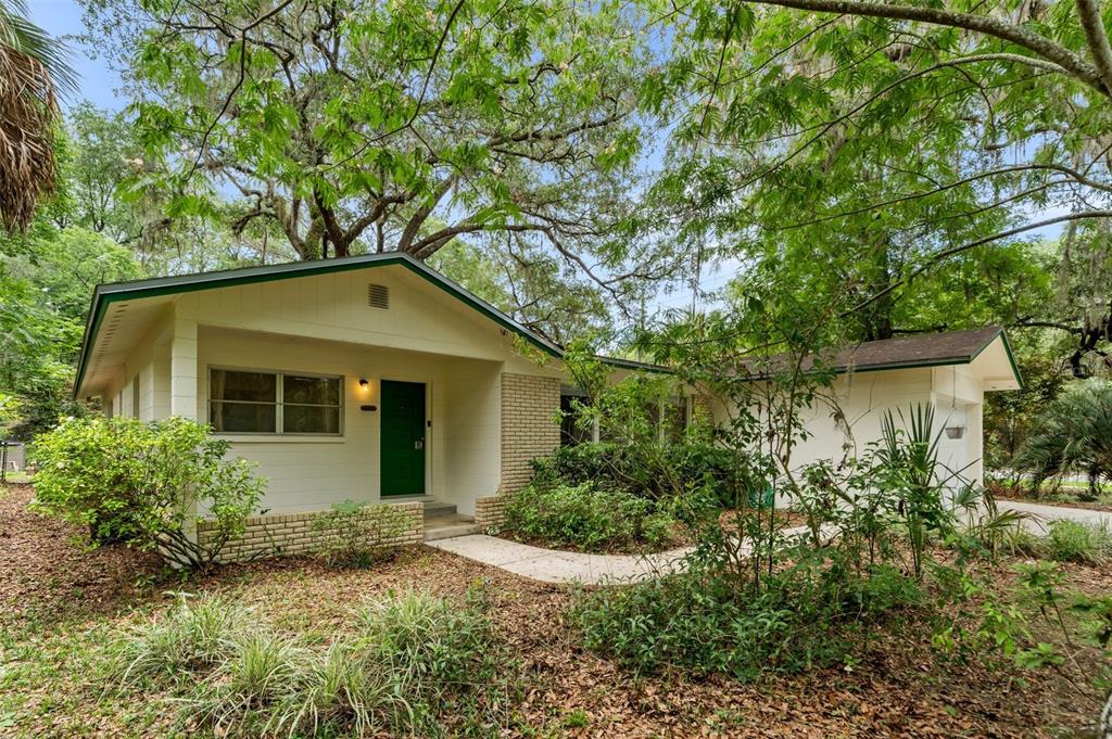A single-story house with a green door, brick accents, and a large tree in front — 805 NW 39TH DRIVE, GAINESVILLE, FL
