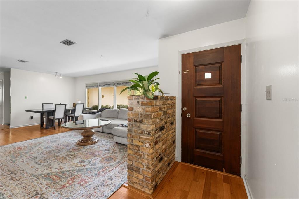 An entryway with a wood door and brick partition opens into a living and dining area — 805 NW 39TH DRIVE, GAINESVILLE, FL