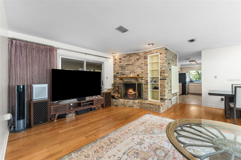 A living room with hardwood floors, a brick fireplace, and a television on a media console — 805 NW 39TH DRIVE, GAINESVILLE, FL