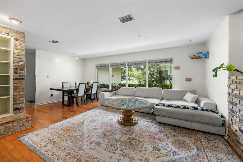 A living and dining room features a sectional sofa, glass coffee table, and brick fireplace — 805 NW 39TH DRIVE, GAINESVILLE, FL