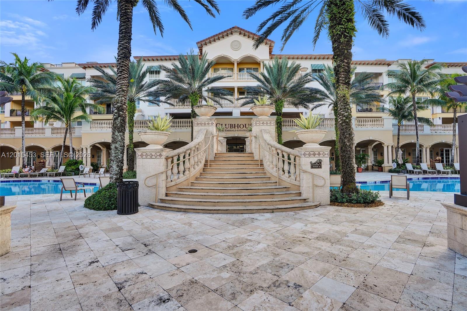A grand stone staircase leads to the entrance of a Mediterranean-style clubhouse with palm trees — 16135 Emerald Estates Dr # 166, Weston FL 33331, WESTON, FL