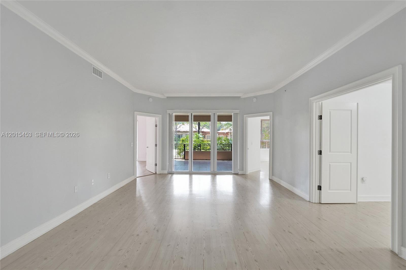 An empty room features light wood-look flooring, white walls, crown molding, and glass sliding doors — 16135 Emerald Estates Dr # 166, Weston FL 33331, WESTON, FL