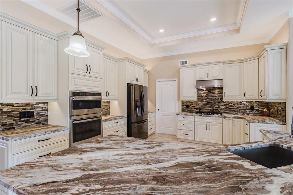 A kitchen features cream-colored cabinets, stainless steel appliances, and a large brown marble island countertop — 1900 NUREMBERG BOULEVARD, PUNTA GORDA, FL