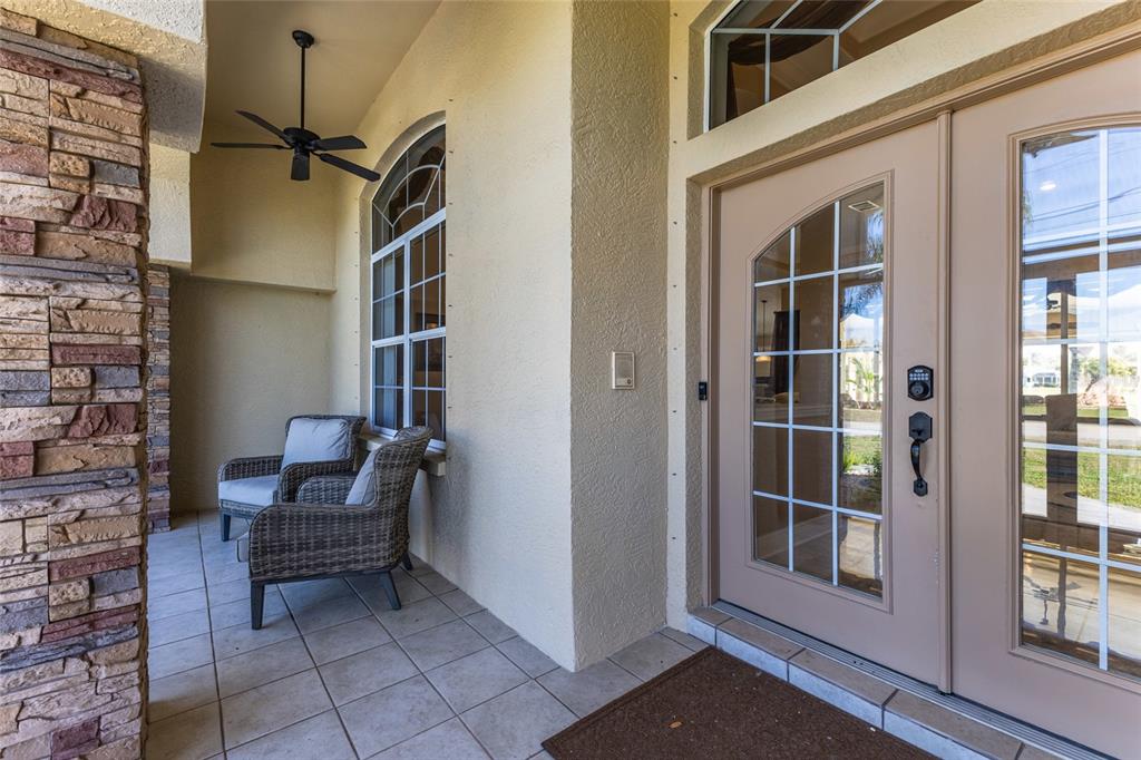 A covered front porch features tiled flooring, two wicker chairs, and a double glass door — 1900 NUREMBERG BOULEVARD, PUNTA GORDA, FL