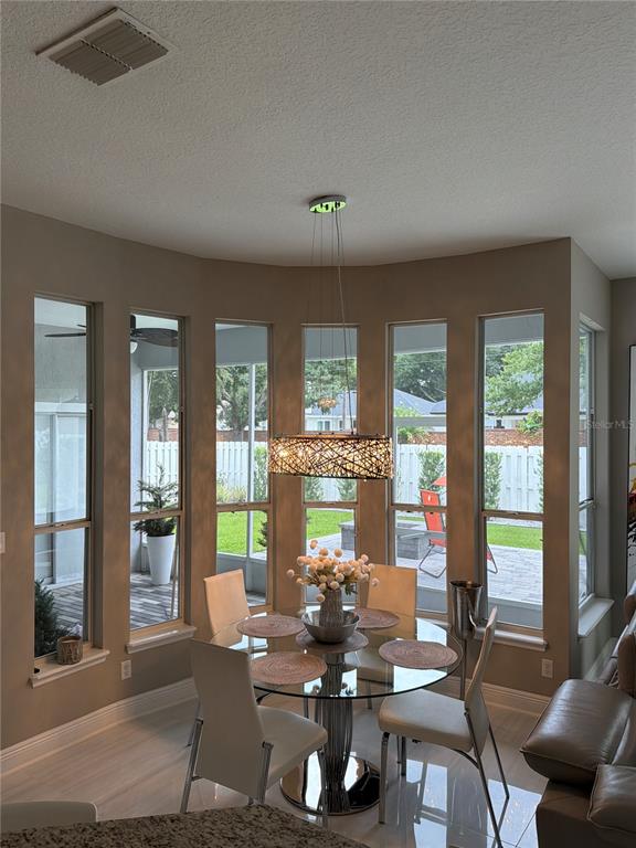 A dining area features a glass table, modern chandelier, and floor-to-ceiling windows overlooking a patio — 10133 FACET COURT, ORLANDO, FL