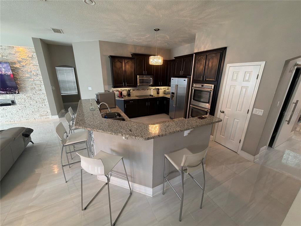 A kitchen features dark wood cabinets, granite countertops, stainless steel appliances, and a breakfast bar — 10133 FACET COURT, ORLANDO, FL