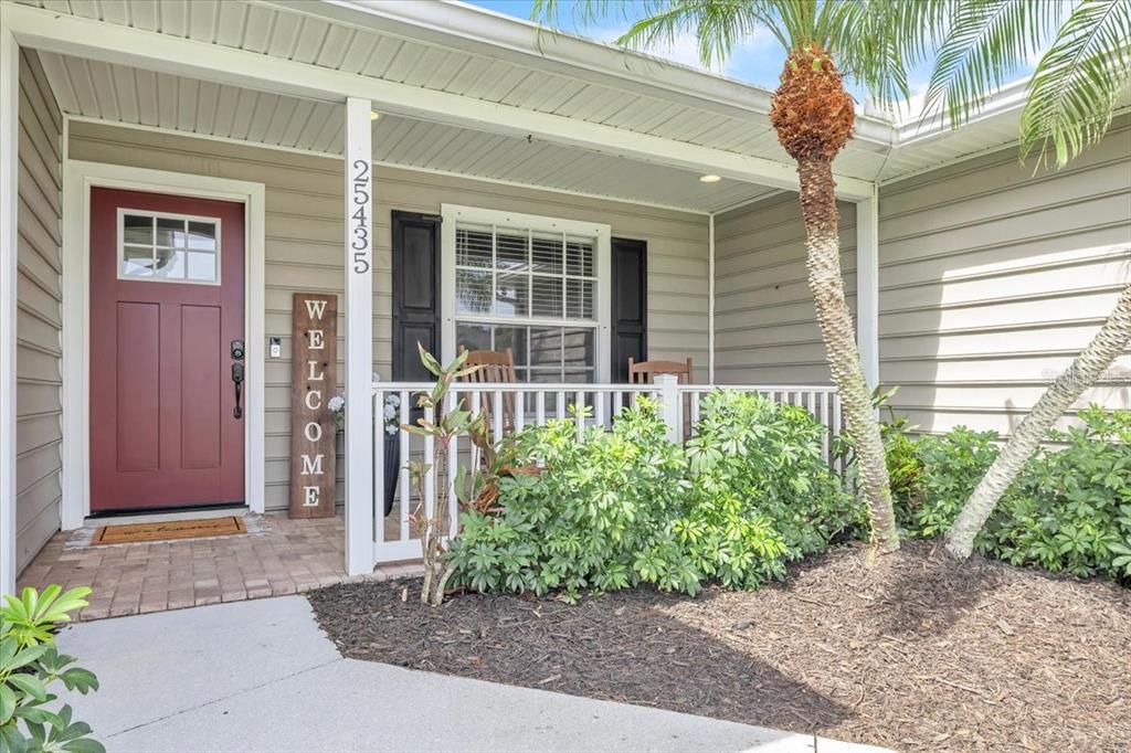 A front porch with a red door, white railing, and a palm tree in the yard — 25435 AREQUIPA DRIVE, PUNTA GORDA, FL