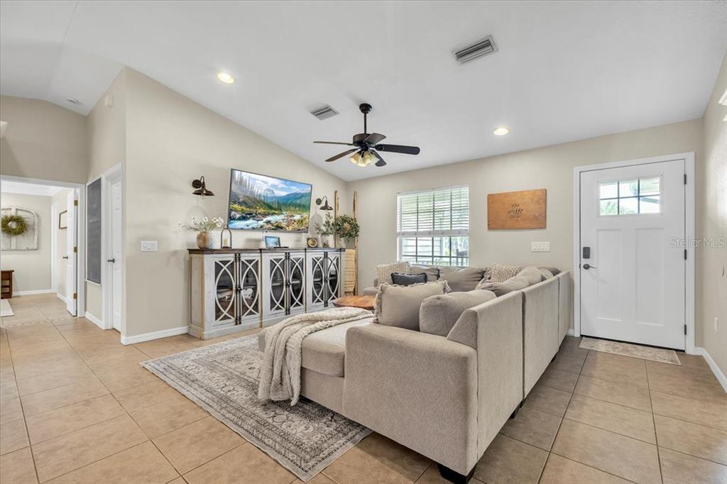 A living room features a sectional sofa, a media console with a television, and tile flooring — 25435 AREQUIPA DRIVE, PUNTA GORDA, FL
