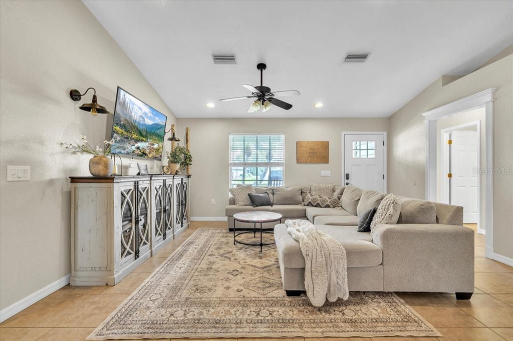 A living room features a large sectional sofa, a patterned area rug, and a media console — 25435 AREQUIPA DRIVE, PUNTA GORDA, FL