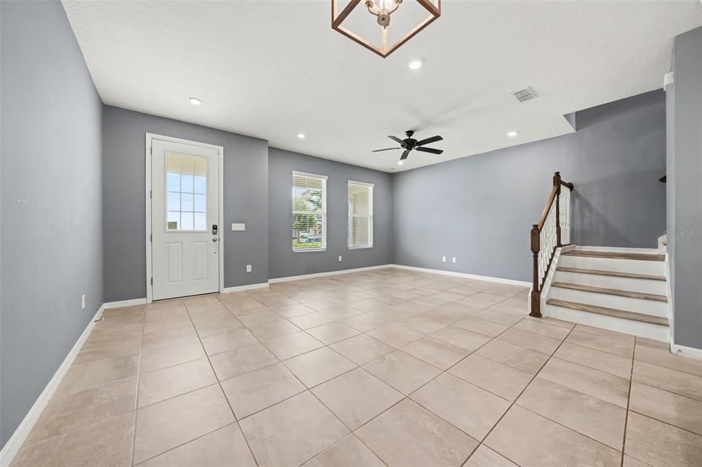 An empty living room features gray walls, tile flooring, a ceiling fan, and a staircase — 1752 FULFILLMENT DRIVE, KISSIMMEE, FL