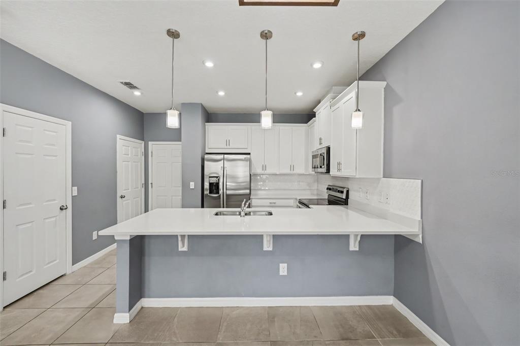 A kitchen features white cabinets, stainless steel appliances, a breakfast bar, and gray walls — 1752 FULFILLMENT DRIVE, KISSIMMEE, FL