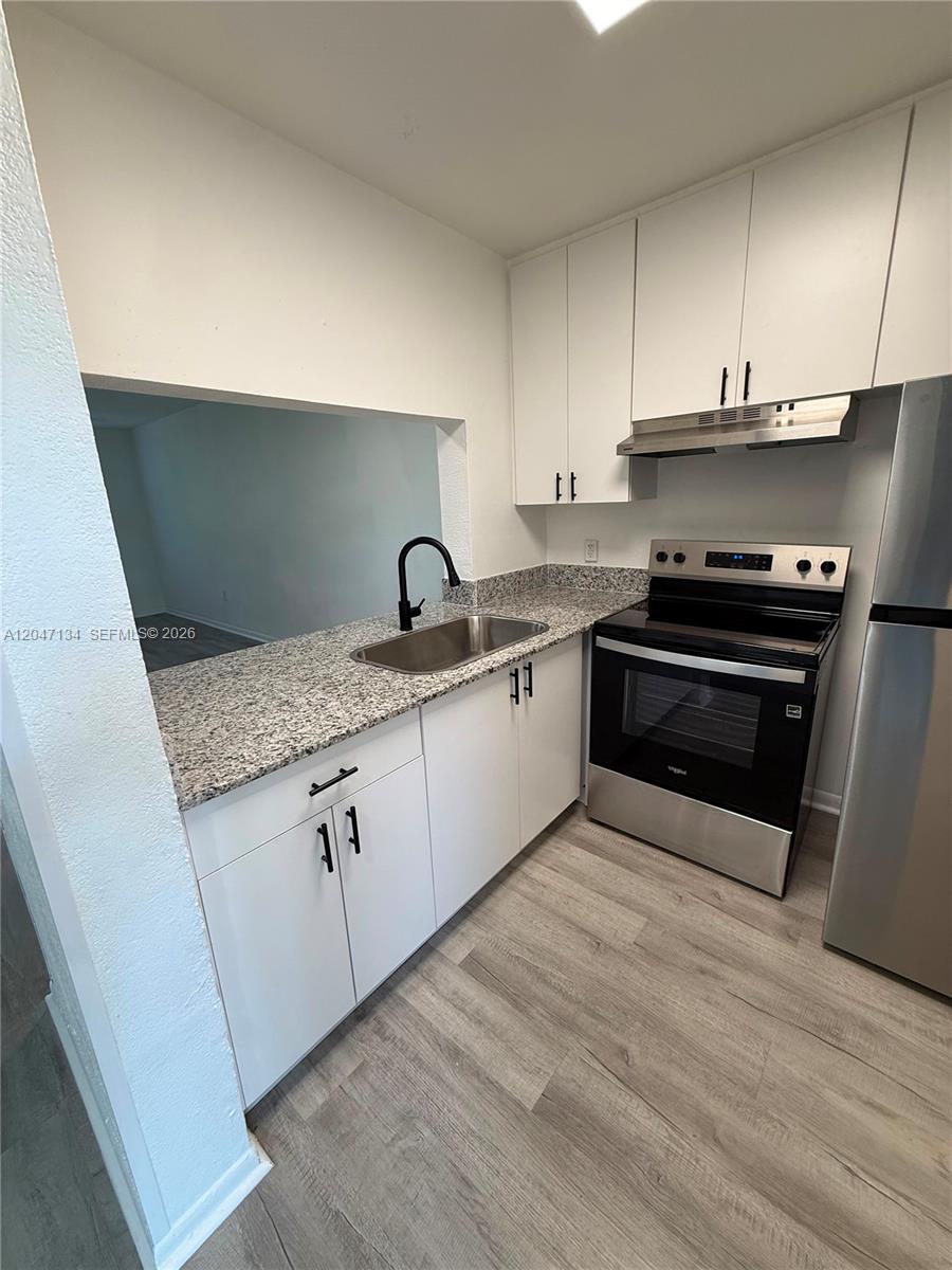 A kitchen features white cabinets, granite countertops, a stainless steel stove, and wood-look flooring — 1220 NW 103rd Ln # 413, Miami FL 33147, MIAMI, FL