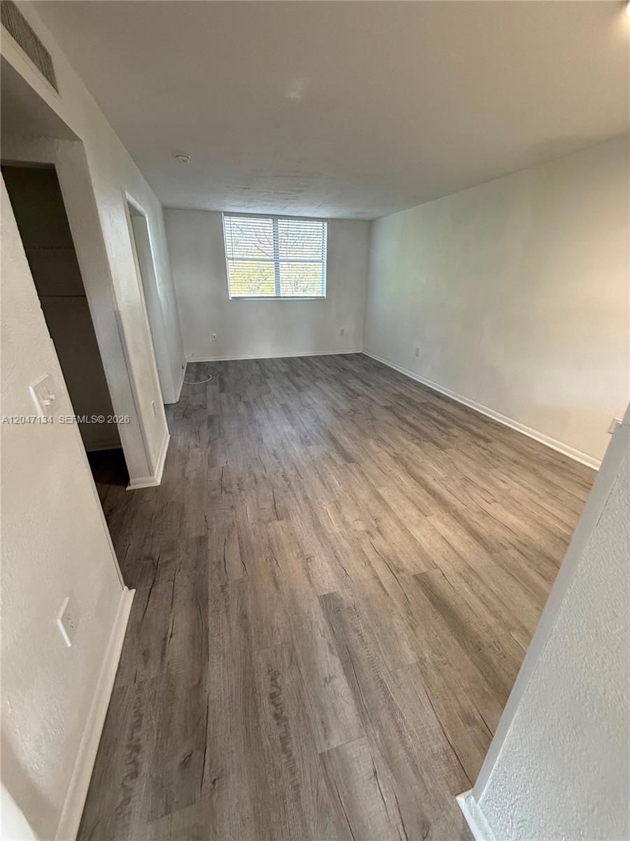 An empty room features light-colored wood-look flooring, white walls, and a single window — 1220 NW 103rd Ln # 413, Miami FL 33147, MIAMI, FL