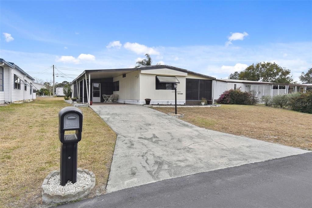 A single-story manufactured home with a concrete driveway, carport, and a front mailbox — 313 MONROE DRIVE, LAKELAND, FL