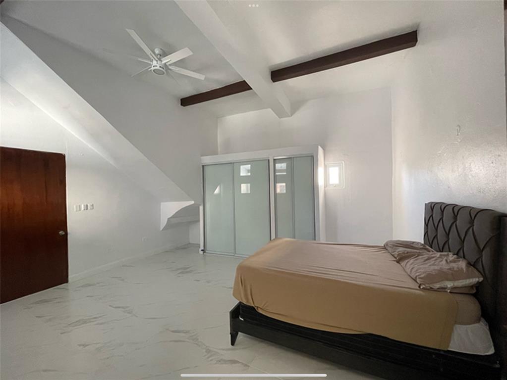 A bedroom with white marble-style flooring, a vaulted ceiling with exposed beams, and a sliding-door closet — 9 DEL MERCADO UNIT 2, SAN JUAN, PR