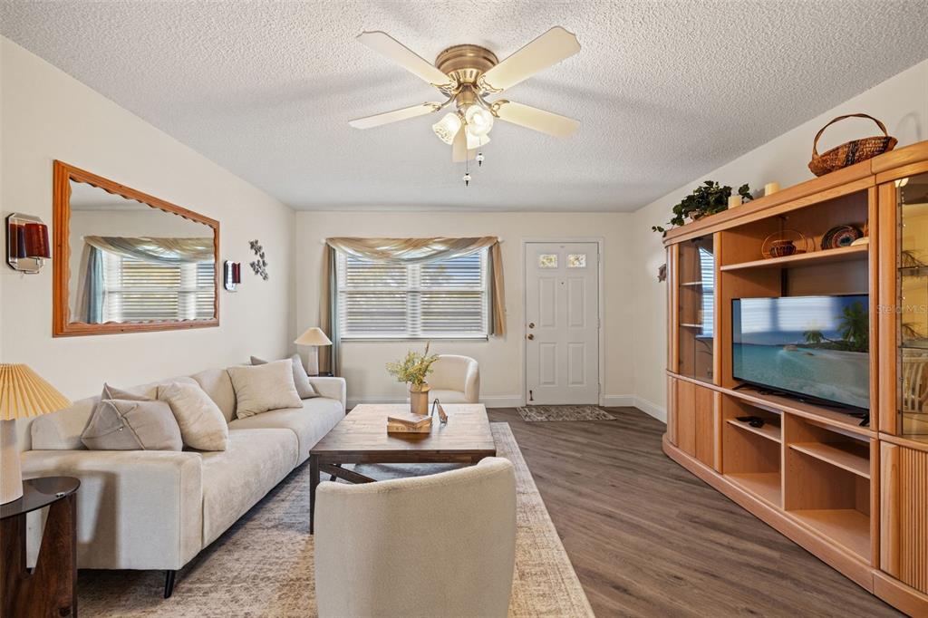 A living room features a beige sofa, wooden coffee table, entertainment center, and ceiling fan — 6070 80TH STREET N UNIT 410, ST PETERSBURG, FL