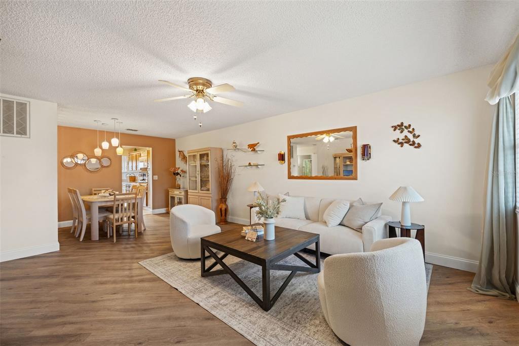 A living room with wood-look flooring, a white sofa, two armchairs, and an adjacent dining area — 6070 80TH STREET N UNIT 410, ST PETERSBURG, FL
