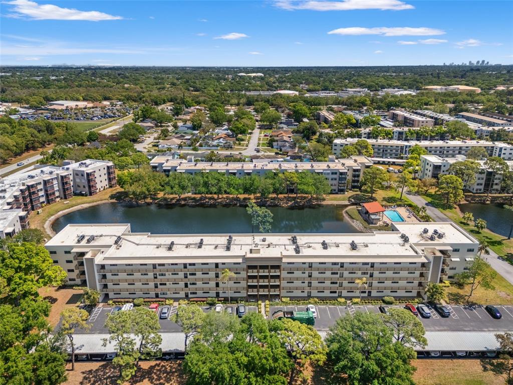 An aerial view shows a multi-story apartment building situated next to a pond and pool — 6070 80TH STREET N UNIT 410, ST PETERSBURG, FL