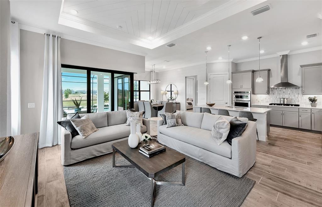 A bright open-concept living room and kitchen featuring light wood floors and neutral furniture — 7452 SUMMER COURT, SARASOTA, FL