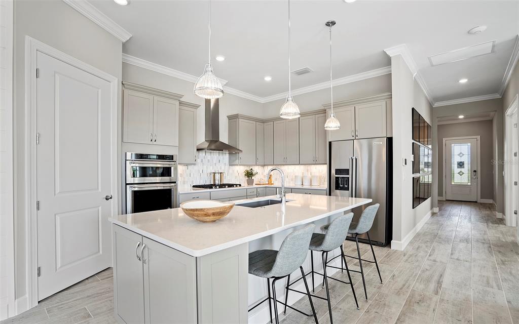 A modern kitchen features light gray cabinetry, a quartz island with bar seating, and stainless appliances — 7452 SUMMER COURT, SARASOTA, FL