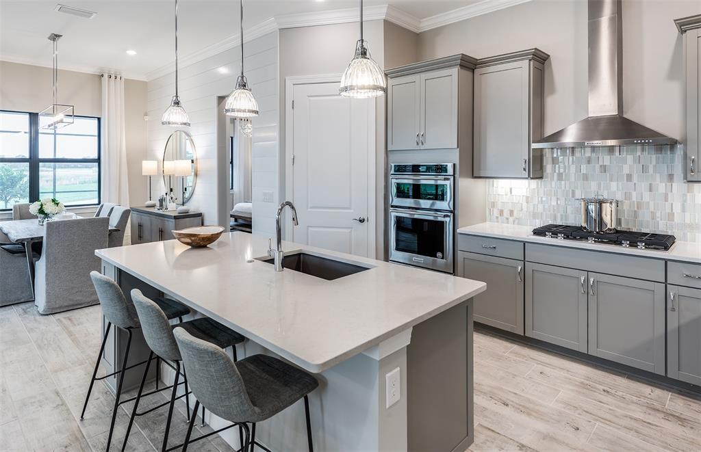 A modern kitchen features a large island, gray cabinetry, stainless steel appliances, and tile flooring — 7452 SUMMER COURT, SARASOTA, FL
