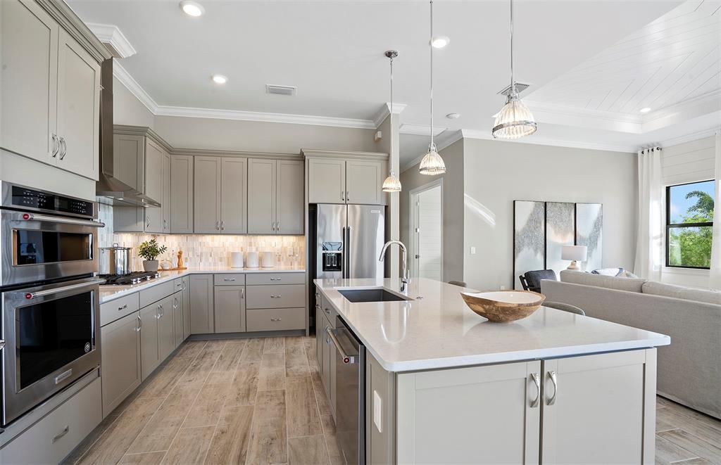 A modern kitchen features gray cabinets, stainless steel appliances, and a large central island — 7452 SUMMER COURT, SARASOTA, FL