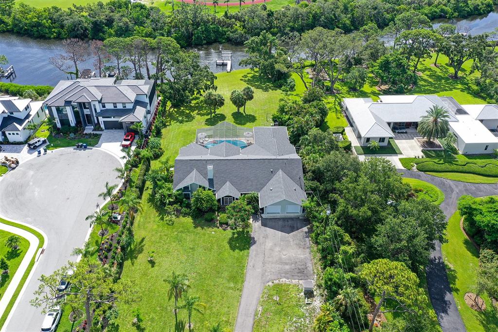 An aerial view shows a house with a pool, driveway, and surrounding green landscape — 4935 RIVERWOOD AVENUE, SARASOTA, FL