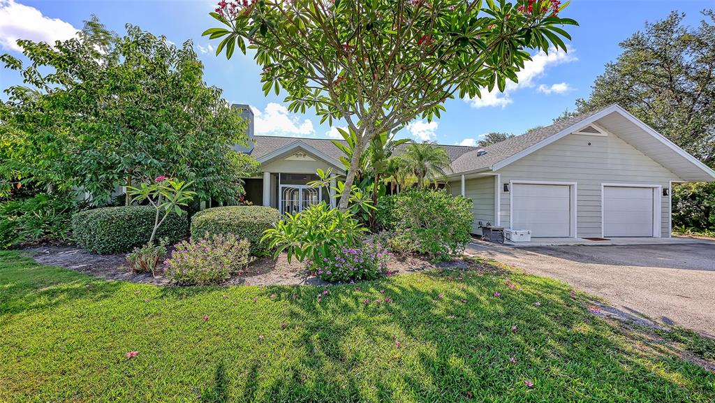 A single-story house with a two-car garage, surrounded by lush landscaping and a large tree — 4935 RIVERWOOD AVENUE, SARASOTA, FL