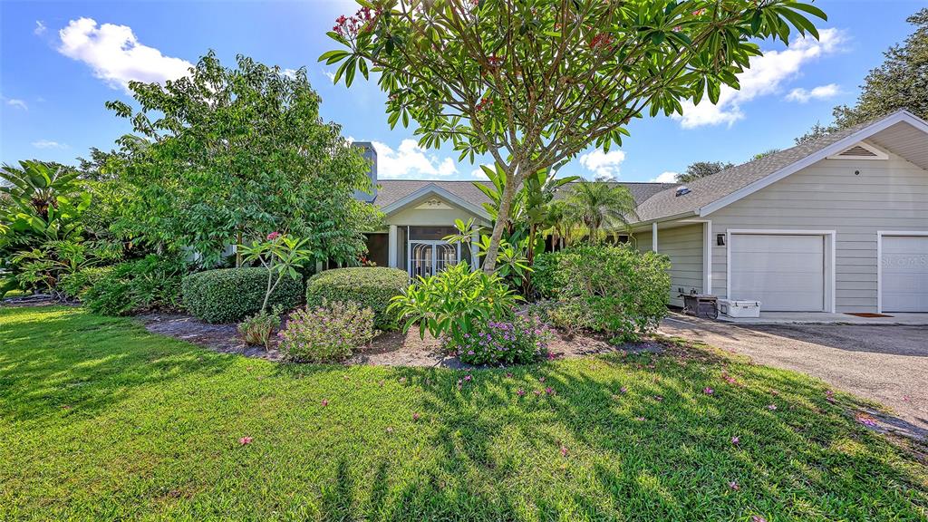 A single-story house with a two-car garage, surrounded by lush landscaping and a green lawn — 4935 RIVERWOOD AVENUE, SARASOTA, FL