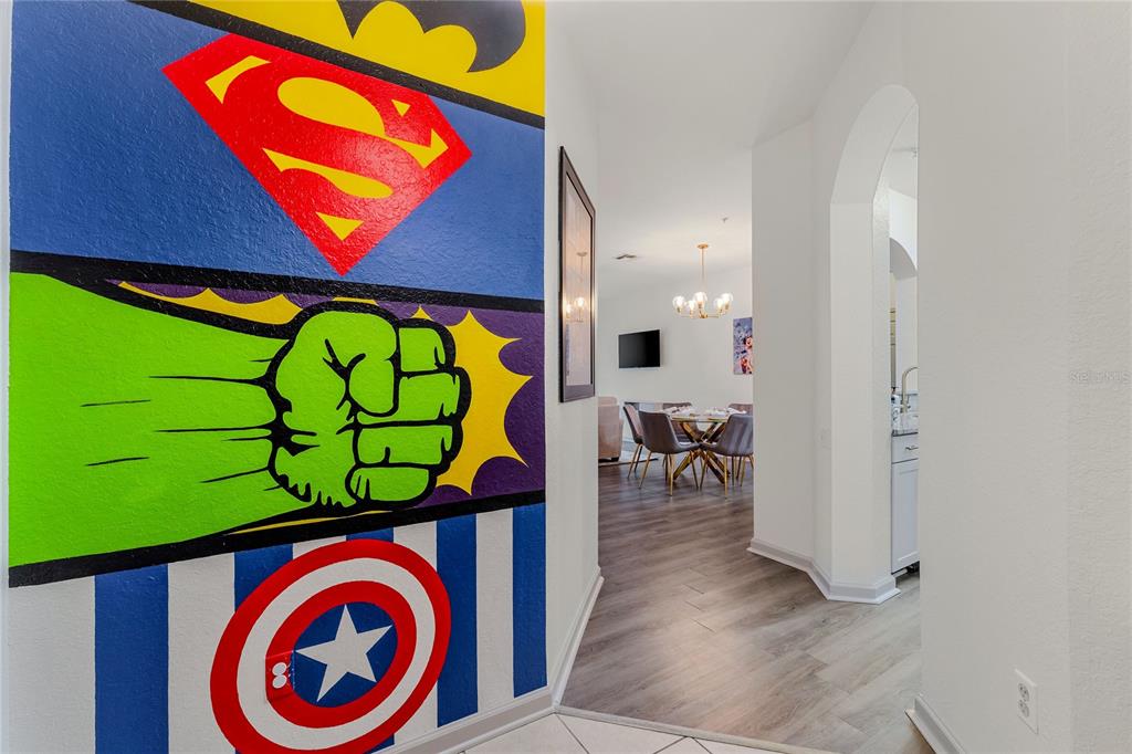 A hallway features a large superhero-themed mural on the wall leading to a dining area — 2774 ALMATON LOOP UNIT 202, KISSIMMEE, FL