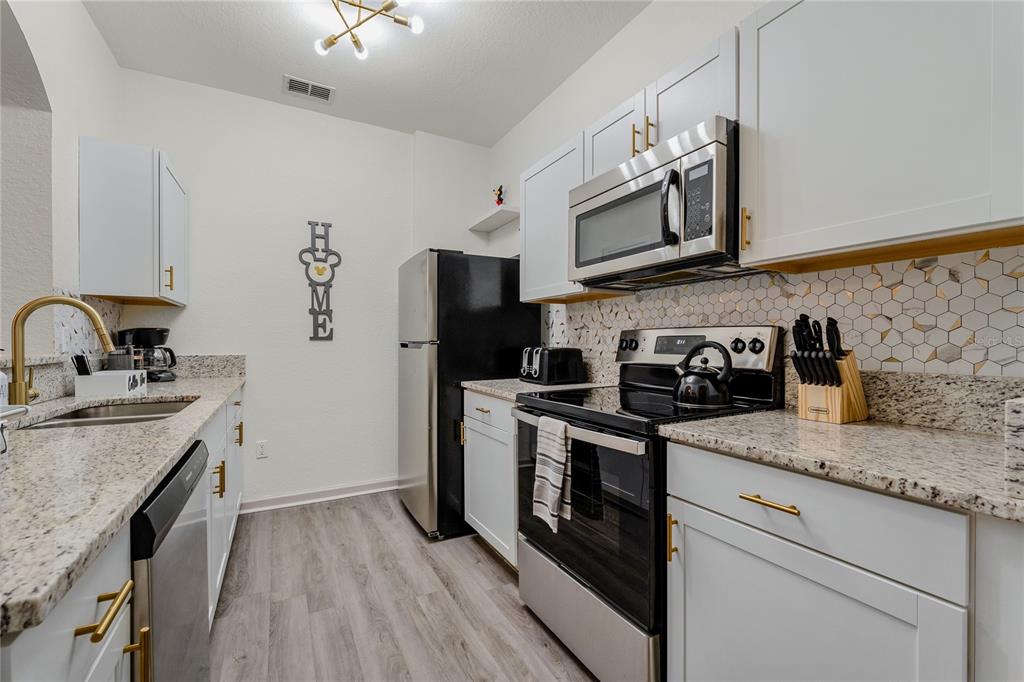 A kitchen features white cabinets, granite countertops, stainless steel appliances, and a hexagonal tile backsplash — 2774 ALMATON LOOP UNIT 202, KISSIMMEE, FL