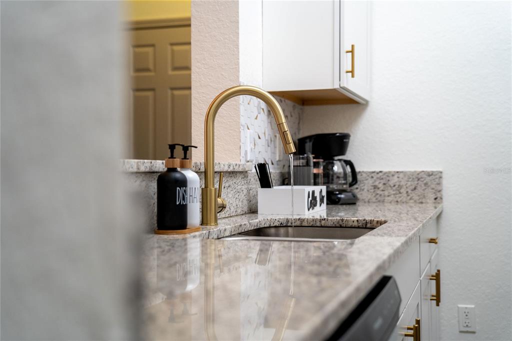 A kitchen sink with a gold faucet and granite countertops sits in front of white cabinets — 2774 ALMATON LOOP UNIT 202, KISSIMMEE, FL
