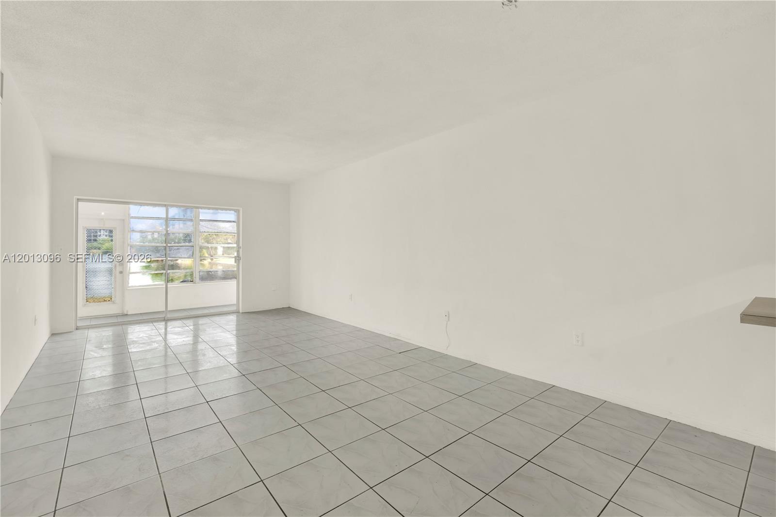 An empty living room features white walls, gray tile flooring, and a sliding glass door — 285 NE 191st St # 2911, Miami FL 33179, MIAMI, FL