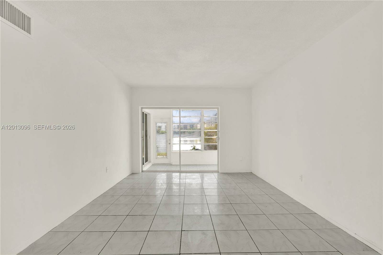 An empty room features white walls, light gray tile flooring, and a sliding glass door — 285 NE 191st St # 2911, Miami FL 33179, MIAMI, FL