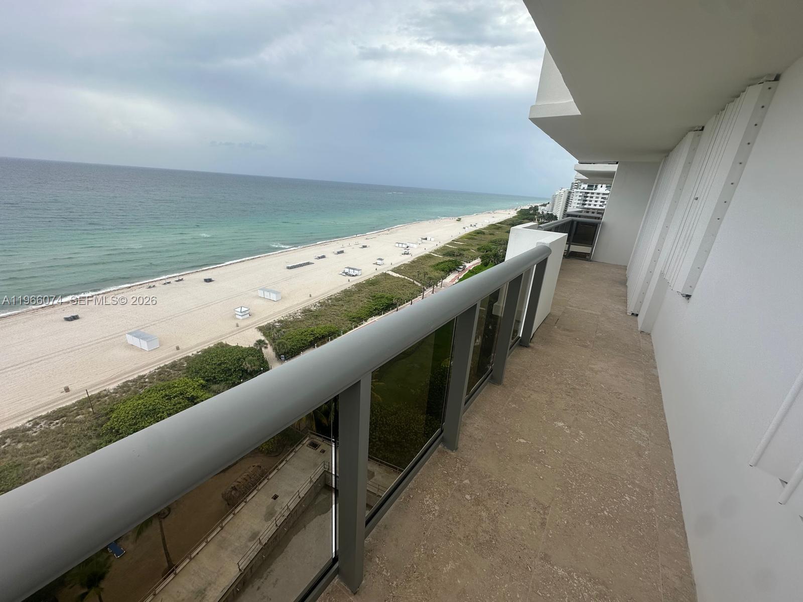 A balcony with a glass railing overlooks a sandy beach and the ocean — 6039 Collins Ave # 1625, Miami Beach FL 33140, MIAMI BEACH, FL