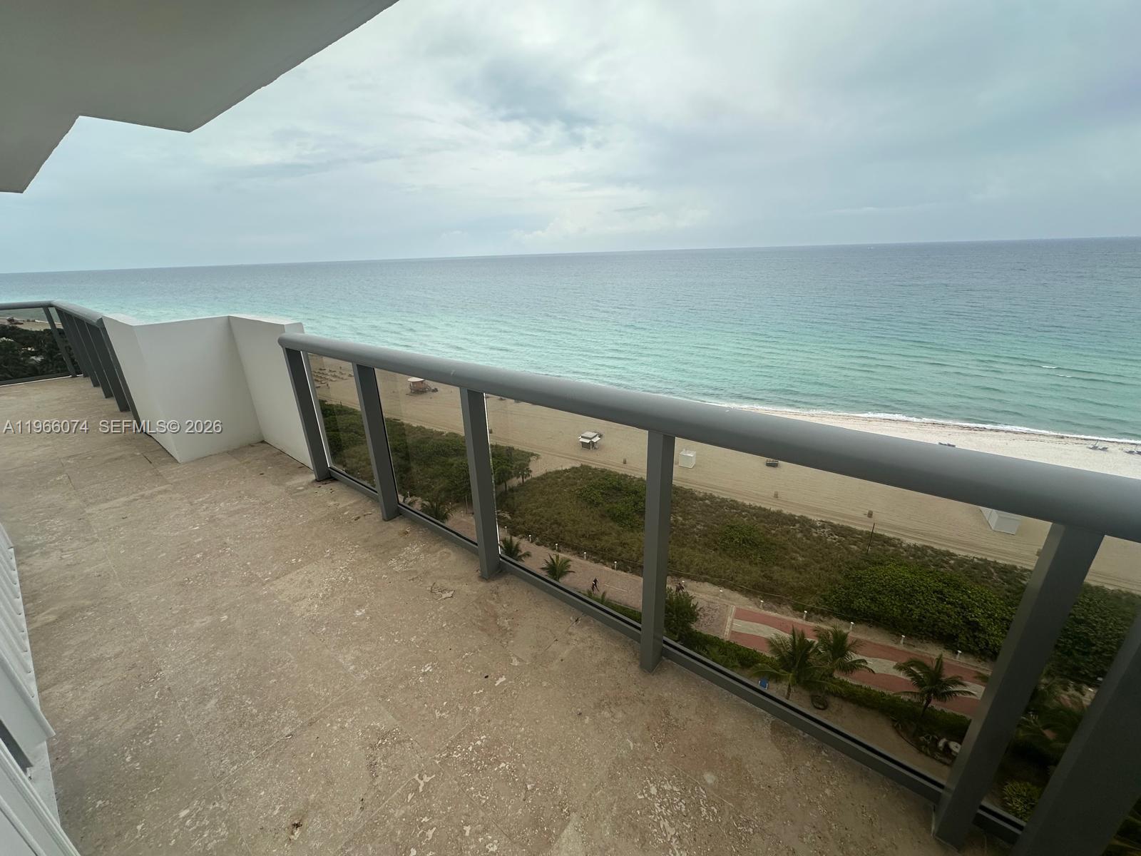 A balcony with stone flooring and a glass railing overlooks the beach and ocean — 6039 Collins Ave # 1625, Miami Beach FL 33140, MIAMI BEACH, FL