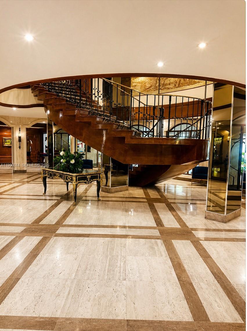 A grand foyer features a curved wooden staircase, marble flooring, and mirrored wall accents — 6039 Collins Ave # 1625, Miami Beach FL 33140, MIAMI BEACH, FL