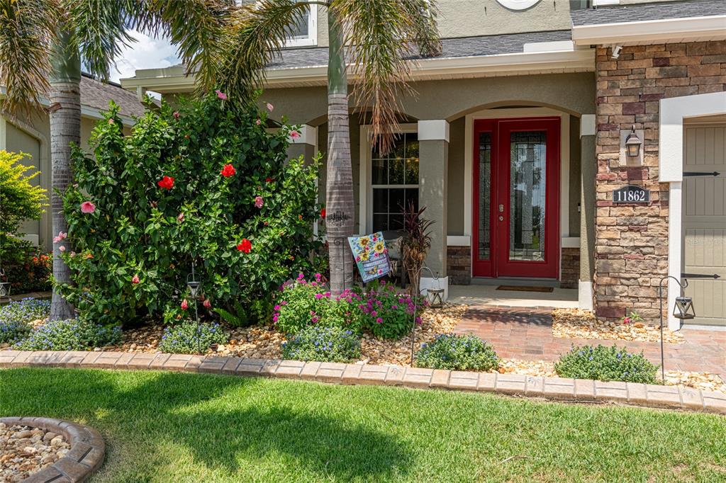The front exterior of a house features a red door, stone siding, and landscaping — 11862 LAKE LUCAYA DRIVE, RIVERVIEW, FL