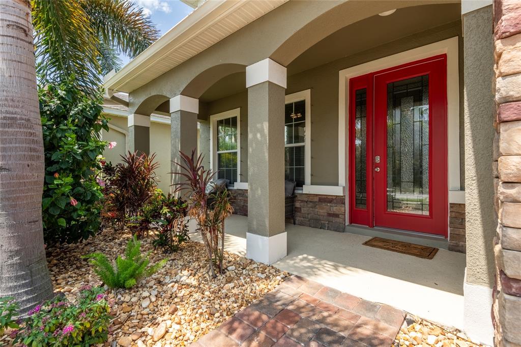 A covered front porch features a bright red door, stone accents, and a landscaped yard — 11862 LAKE LUCAYA DRIVE, RIVERVIEW, FL