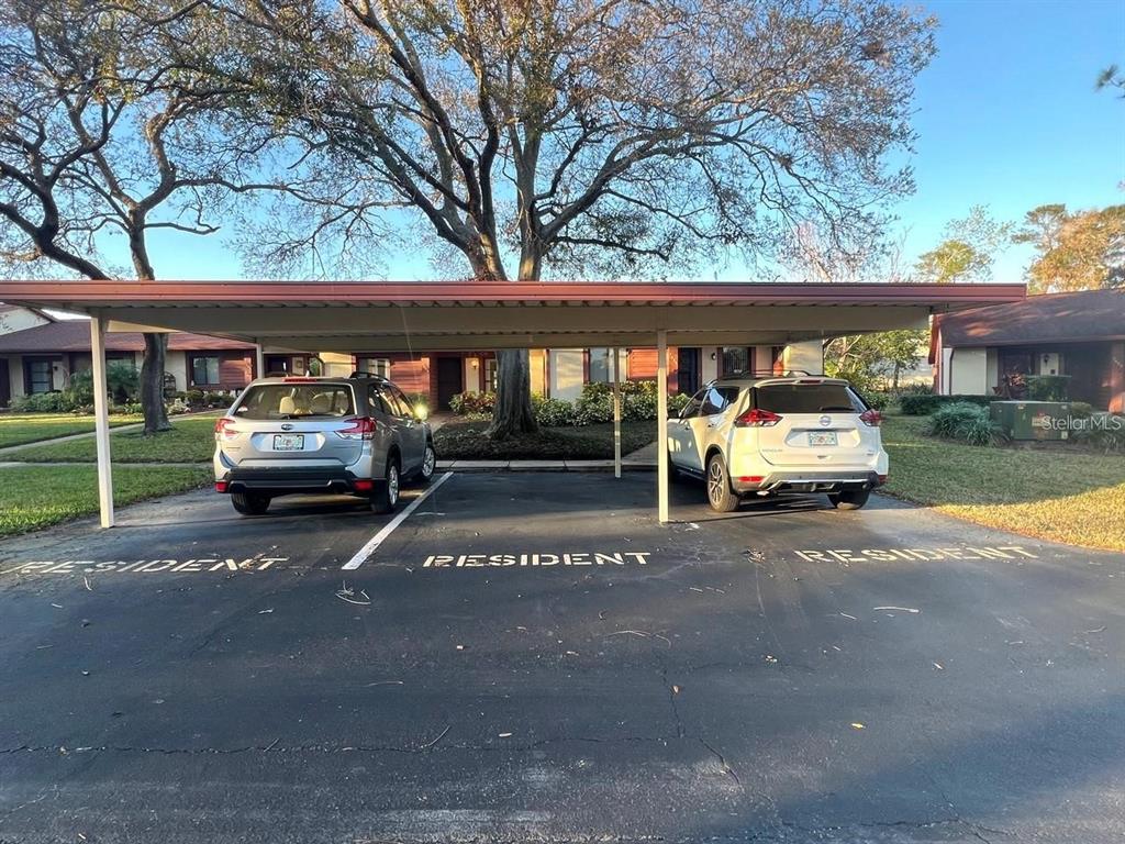 Two cars are parked under a covered carport in front of a residential building — 7523 GREYSTONE DRIVE, HUDSON, FL