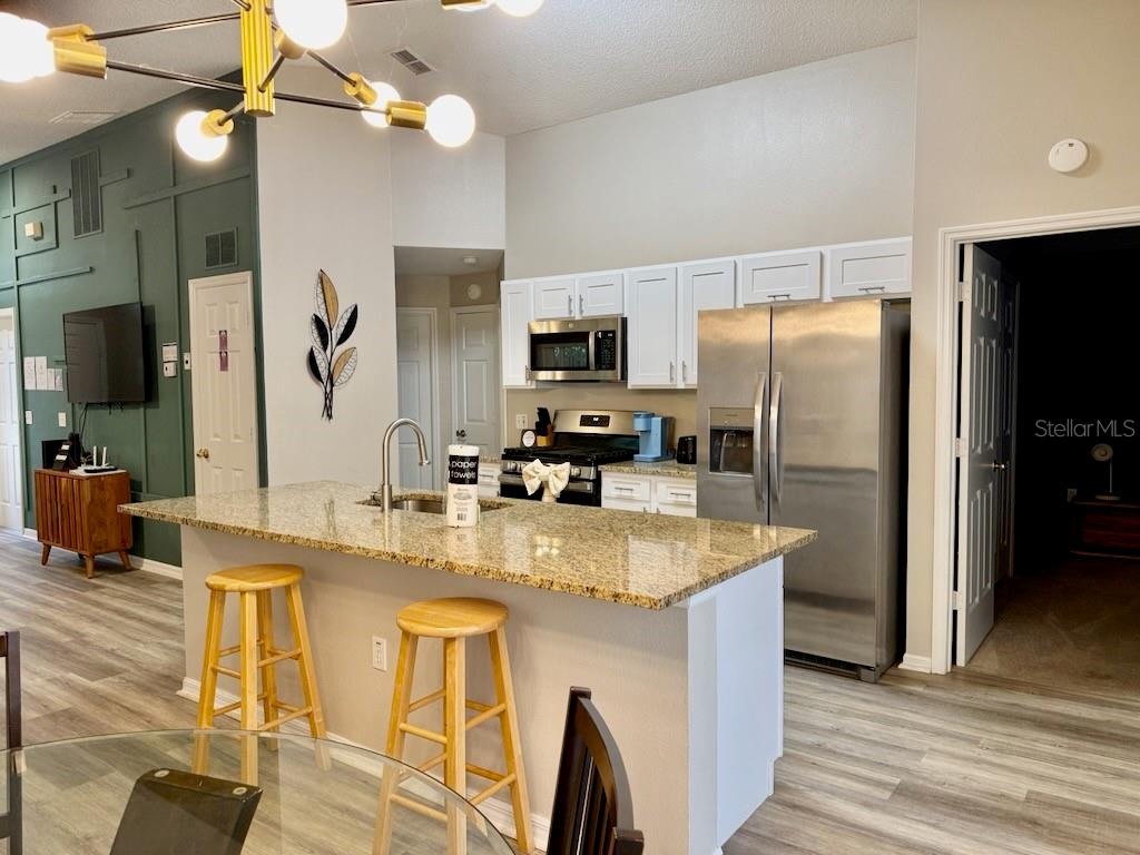 A kitchen features a granite-topped island with bar stools, white cabinetry, and stainless steel appliances — 131 SONJA CIRCLE, DAVENPORT, FL