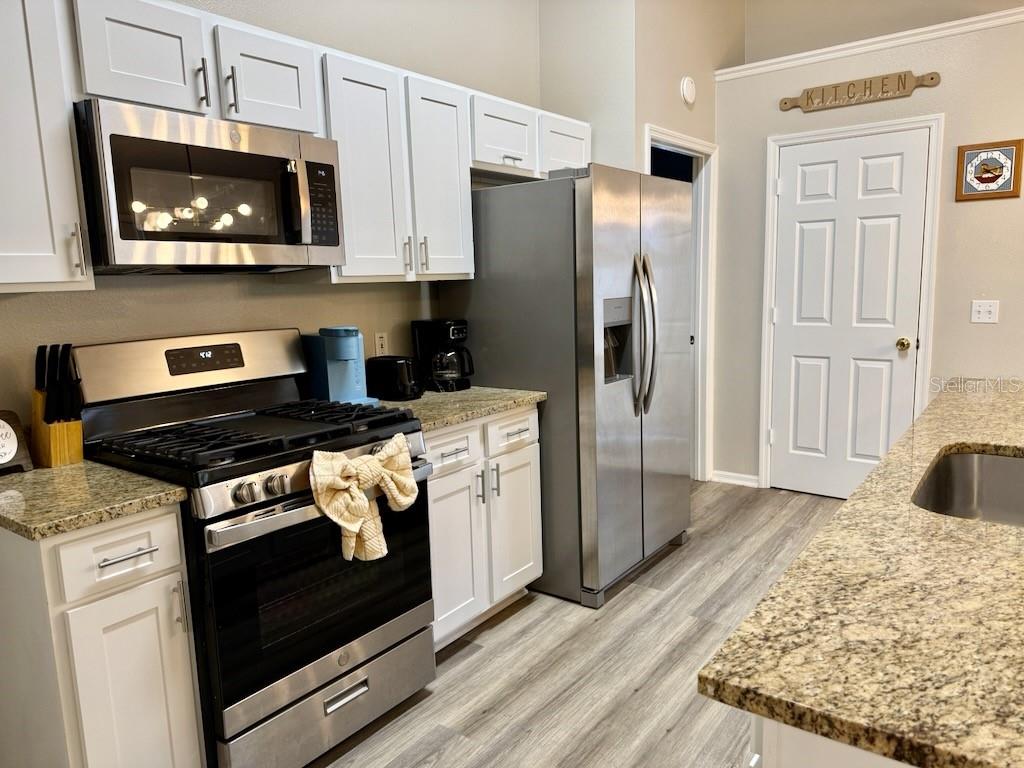 A kitchen features white cabinets, stainless steel appliances, granite countertops, and light wood-look flooring — 131 SONJA CIRCLE, DAVENPORT, FL