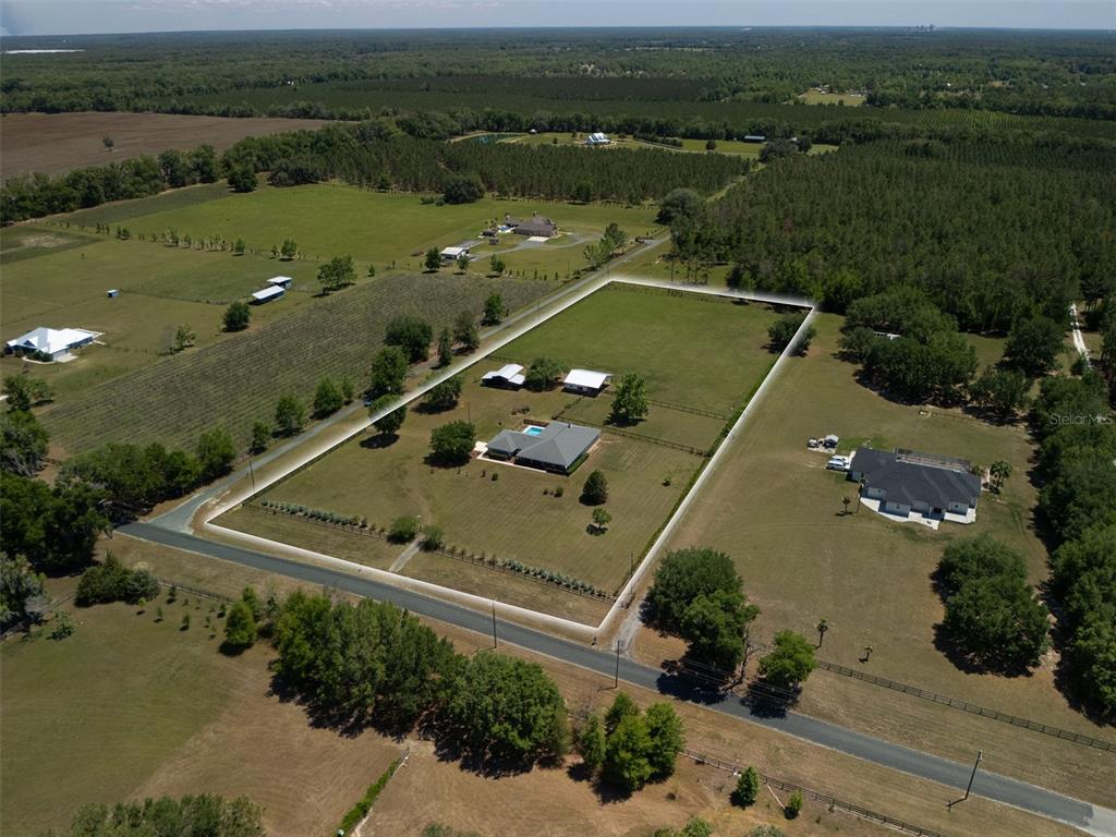 An aerial view shows a fenced residential property featuring a house with a pool — 23053 NW 142ND AVENUE, HIGH SPRINGS, FL