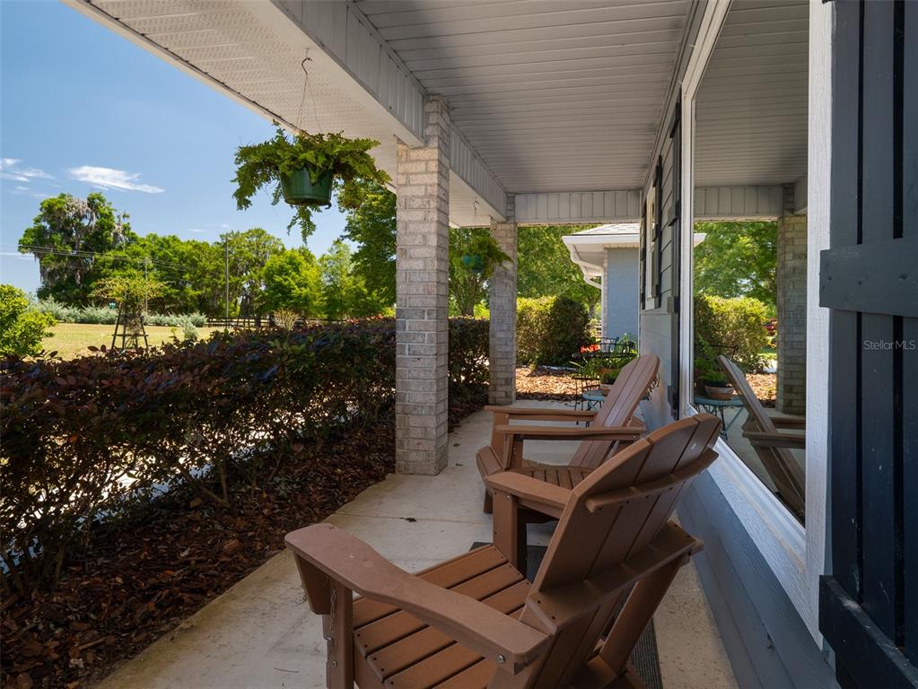 A covered porch features two wooden Adirondack chairs, brick columns, and a hanging plant — 23053 NW 142ND AVENUE, HIGH SPRINGS, FL