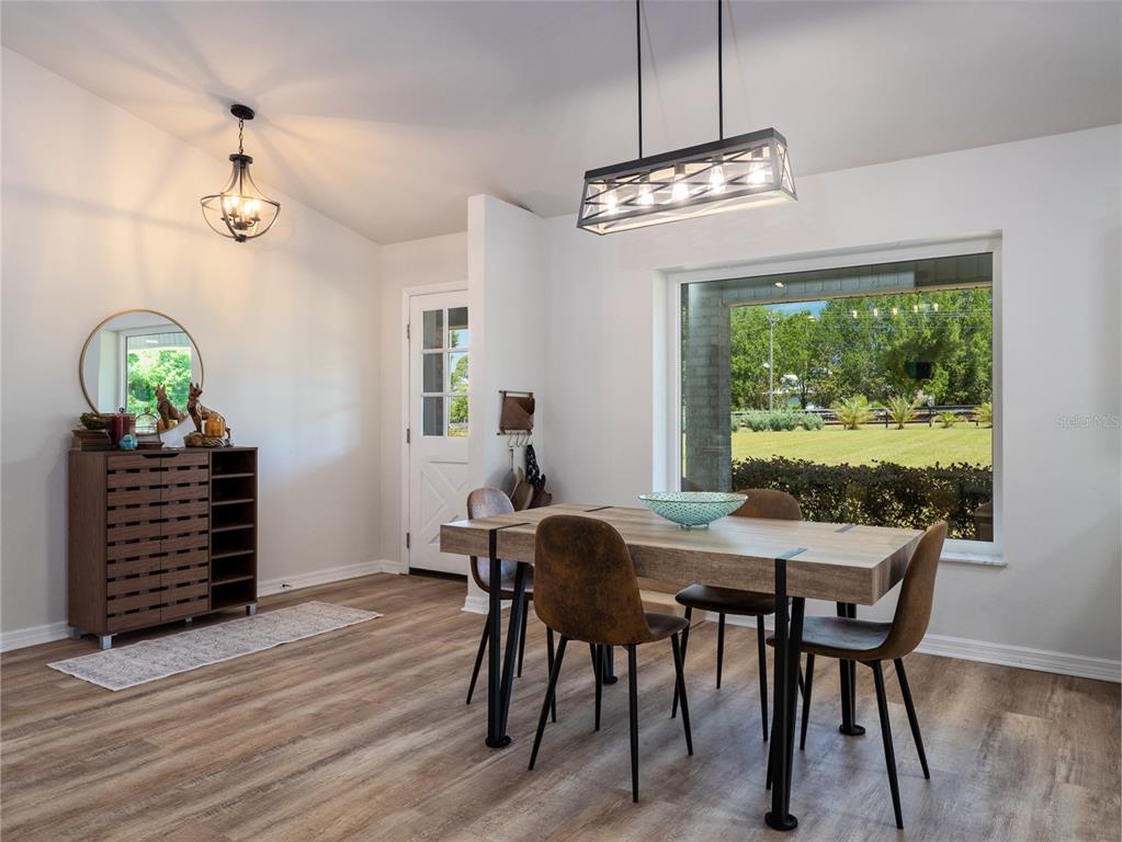 A dining room features a wooden table, four chairs, two light fixtures, and a large window — 23053 NW 142ND AVENUE, HIGH SPRINGS, FL