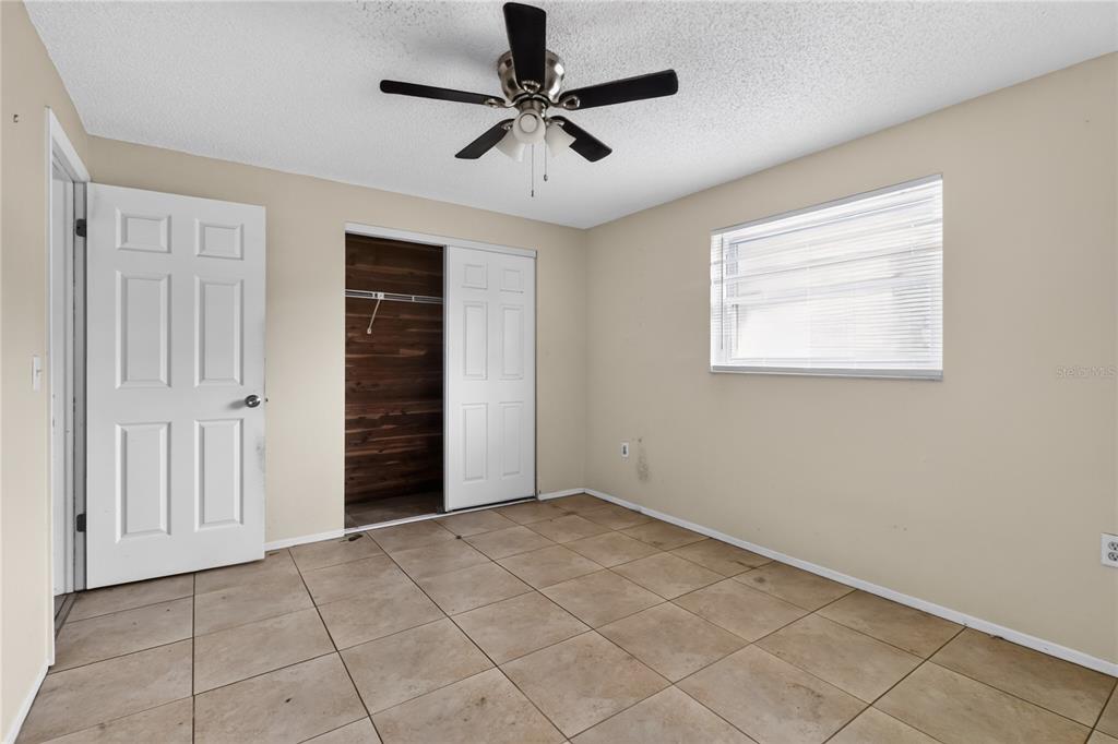 A bedroom with beige walls, tile flooring, a ceiling fan, and a wood-paneled closet — 7036 ASHWOOD DRIVE, PORT RICHEY, FL