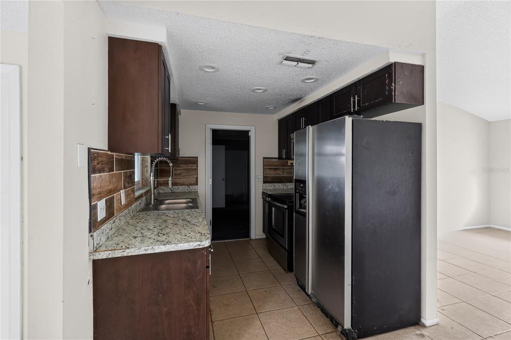 A kitchen features dark wood cabinets, granite countertops, a stainless steel refrigerator, and tiled flooring — 7036 ASHWOOD DRIVE, PORT RICHEY, FL