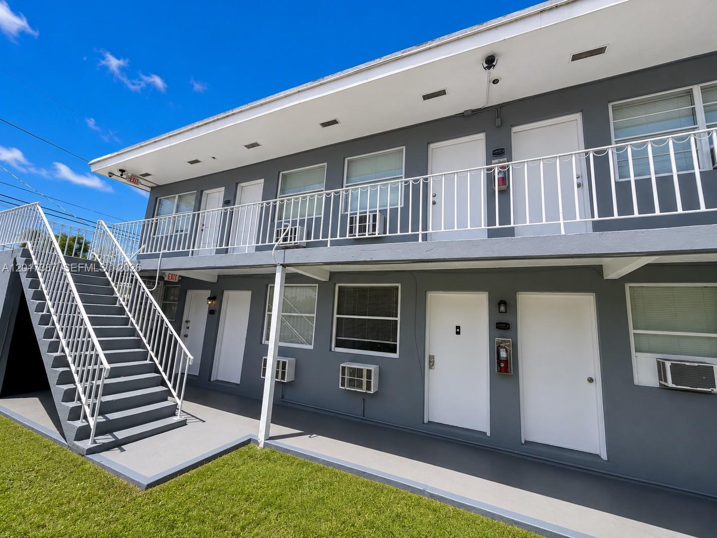 A two-story gray apartment building features exterior staircases, white railings, and multiple unit doors — 1761 Ali Baba Ave, Opa-Locka FL 33054, OPA-LOCKA, FL